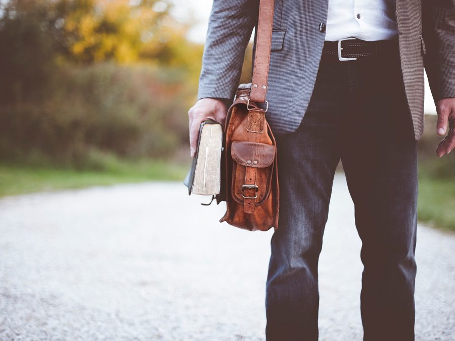 A man walking down a country path carrying a book