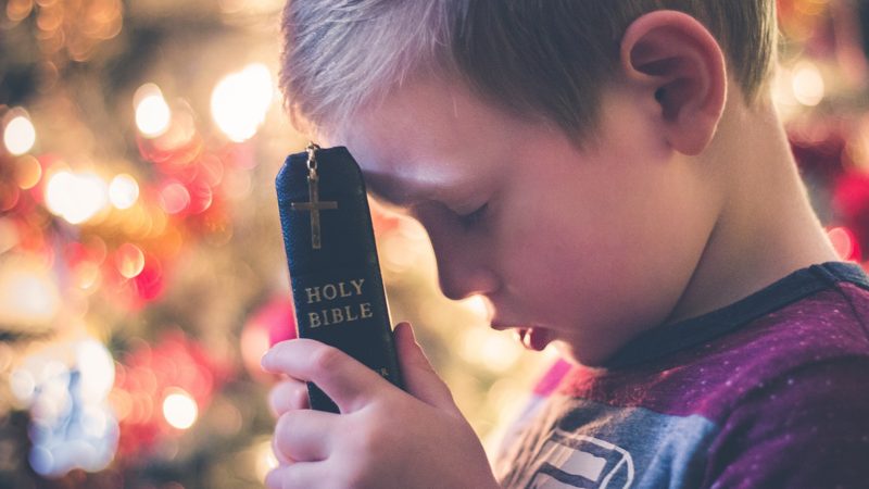 A boy praying with a Bible held to his forehead